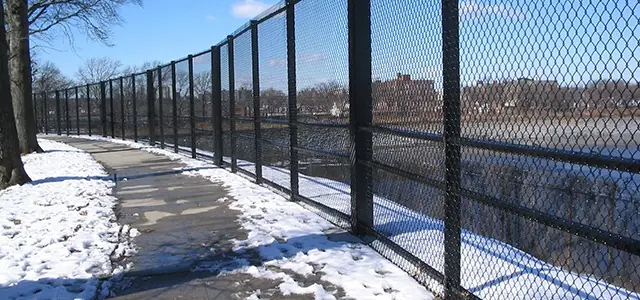 Chain-link fence runs alongside a snow-covered path by a riverside.