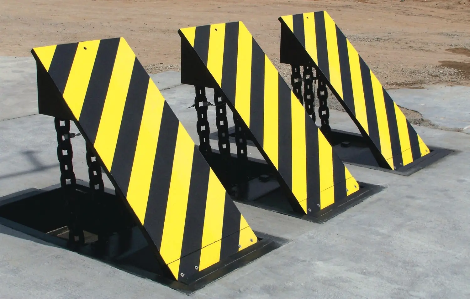 Three wedge-shaped barriers with yellow and black stripes stand upright on an outdoor concrete surface.