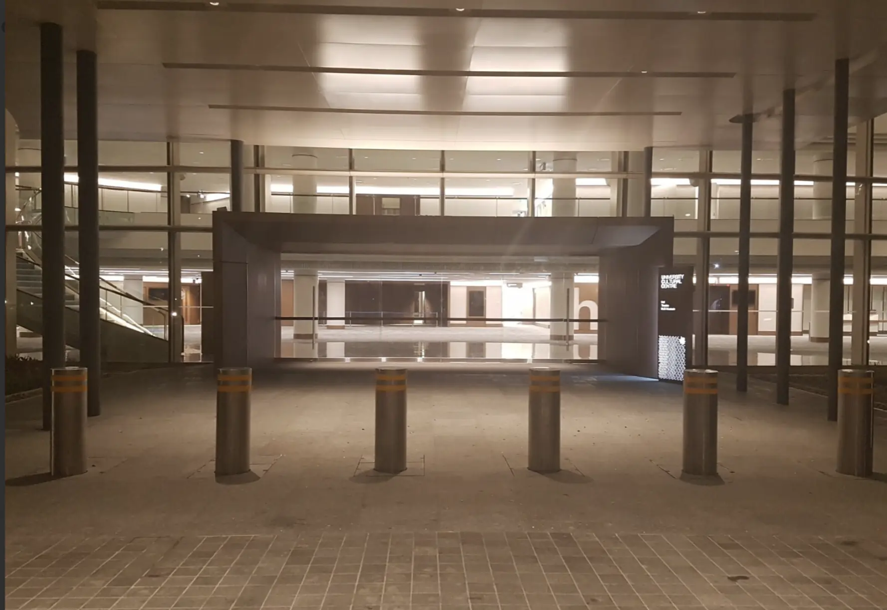 Steel bollards with yellow stripes guard the entryway of a brightly illuminated building lobby.