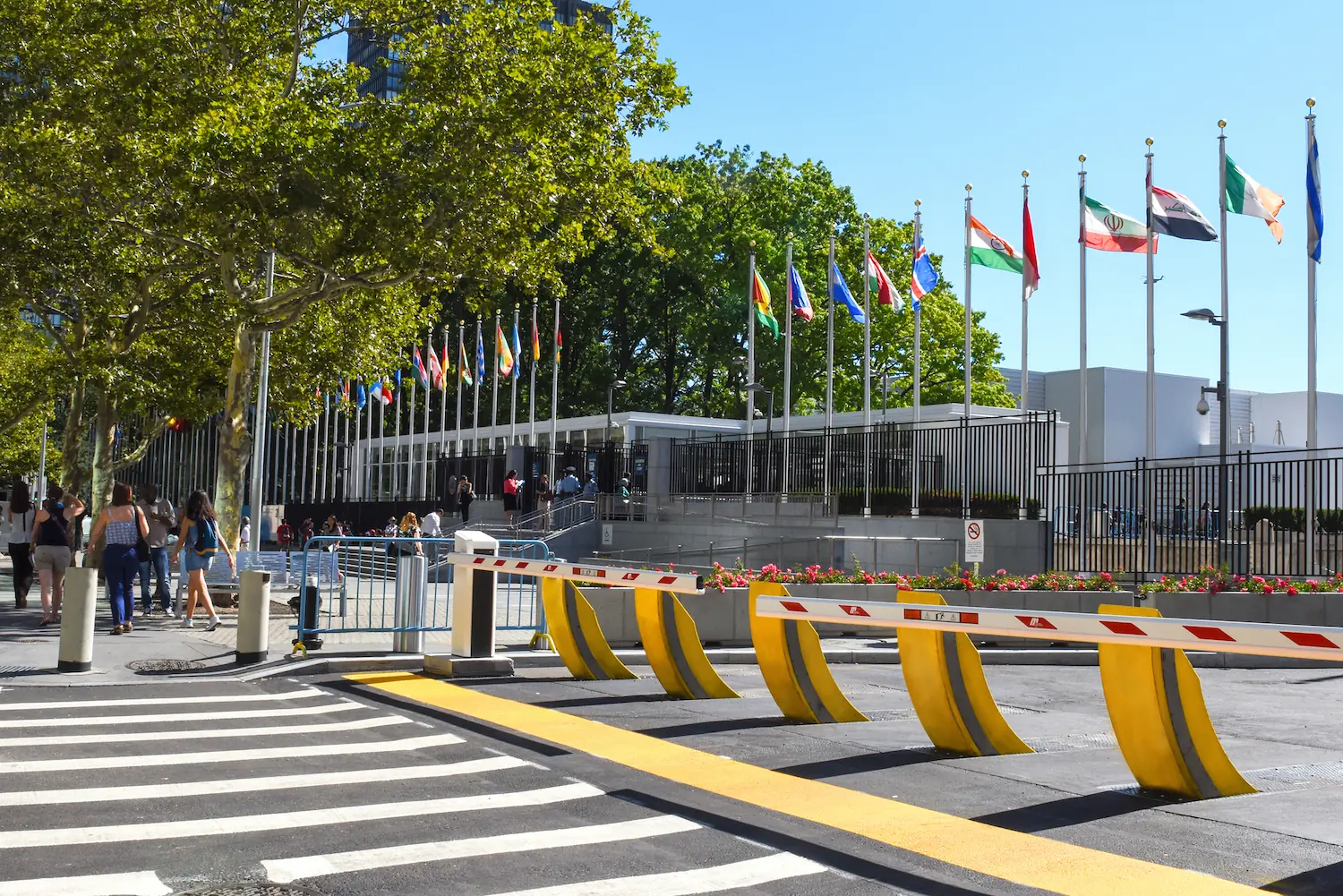 Security barriers and yellow Raptor bollards at an international building with flags.