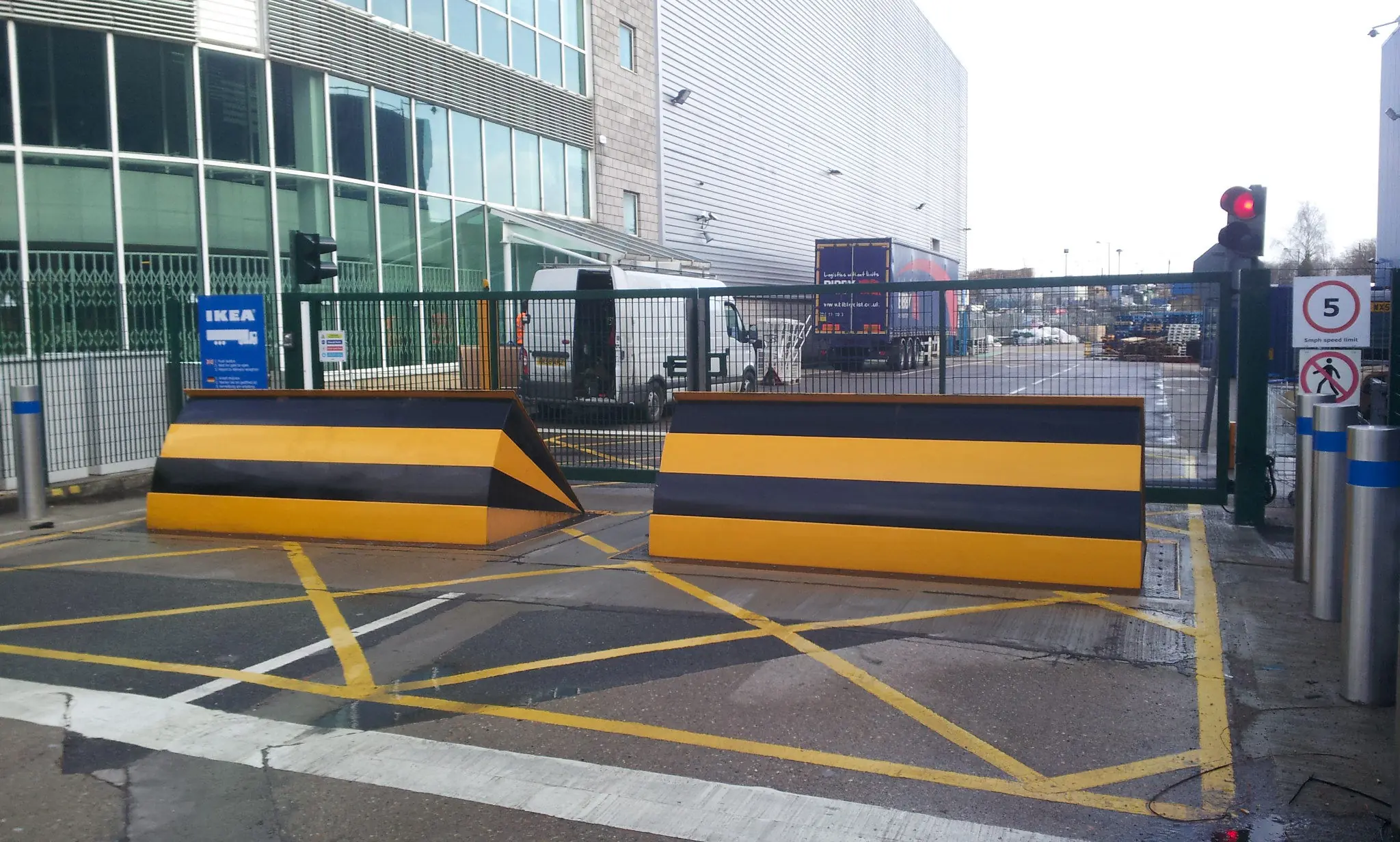 Two large yellow and black wedge barriers positioned at a gated facility entrance with marked lines on the pavement.