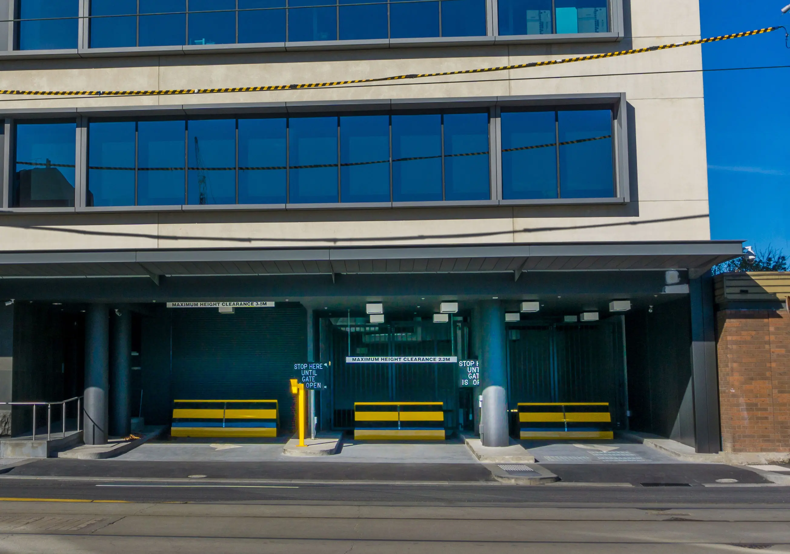 Three yellow and black wedge barriers guard the entry of an underground parking facility with signs indicating height clearance.