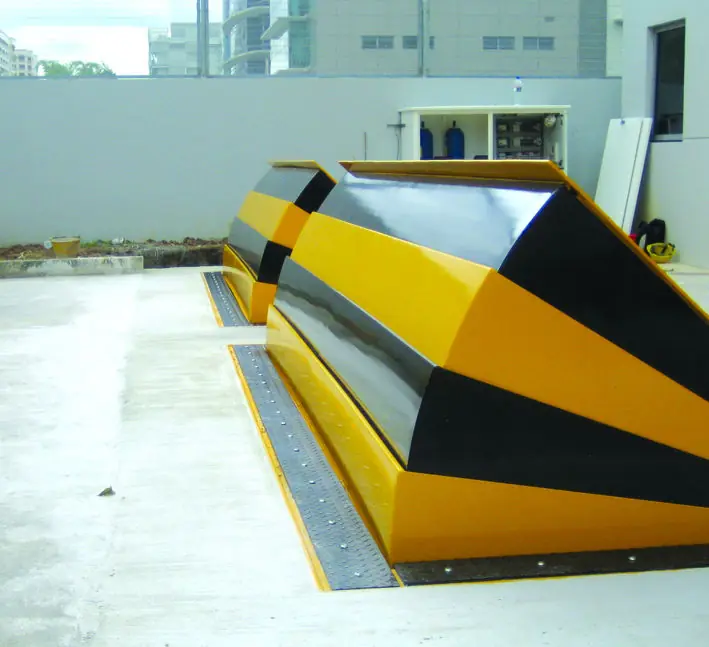 Detailed view of a yellow-striped wedge barrier designed for vehicle access control and installed on a driveway.