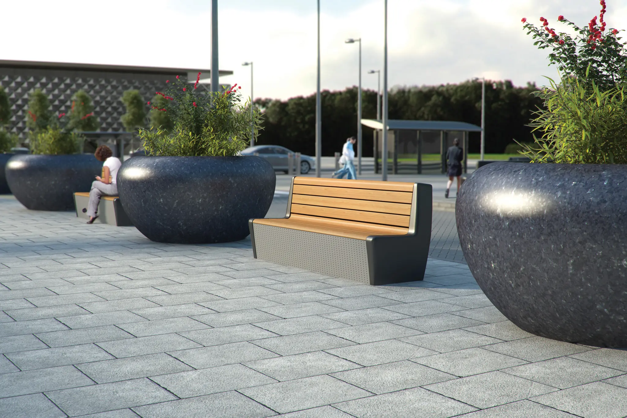 Wooden benches and large round planters with greenery line a paved public plaza.