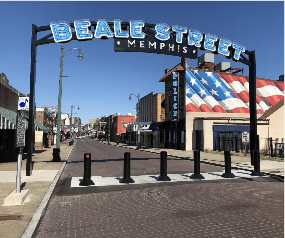 Black bollards blocking vehicle access to Beale Street under an archway with neon signage.