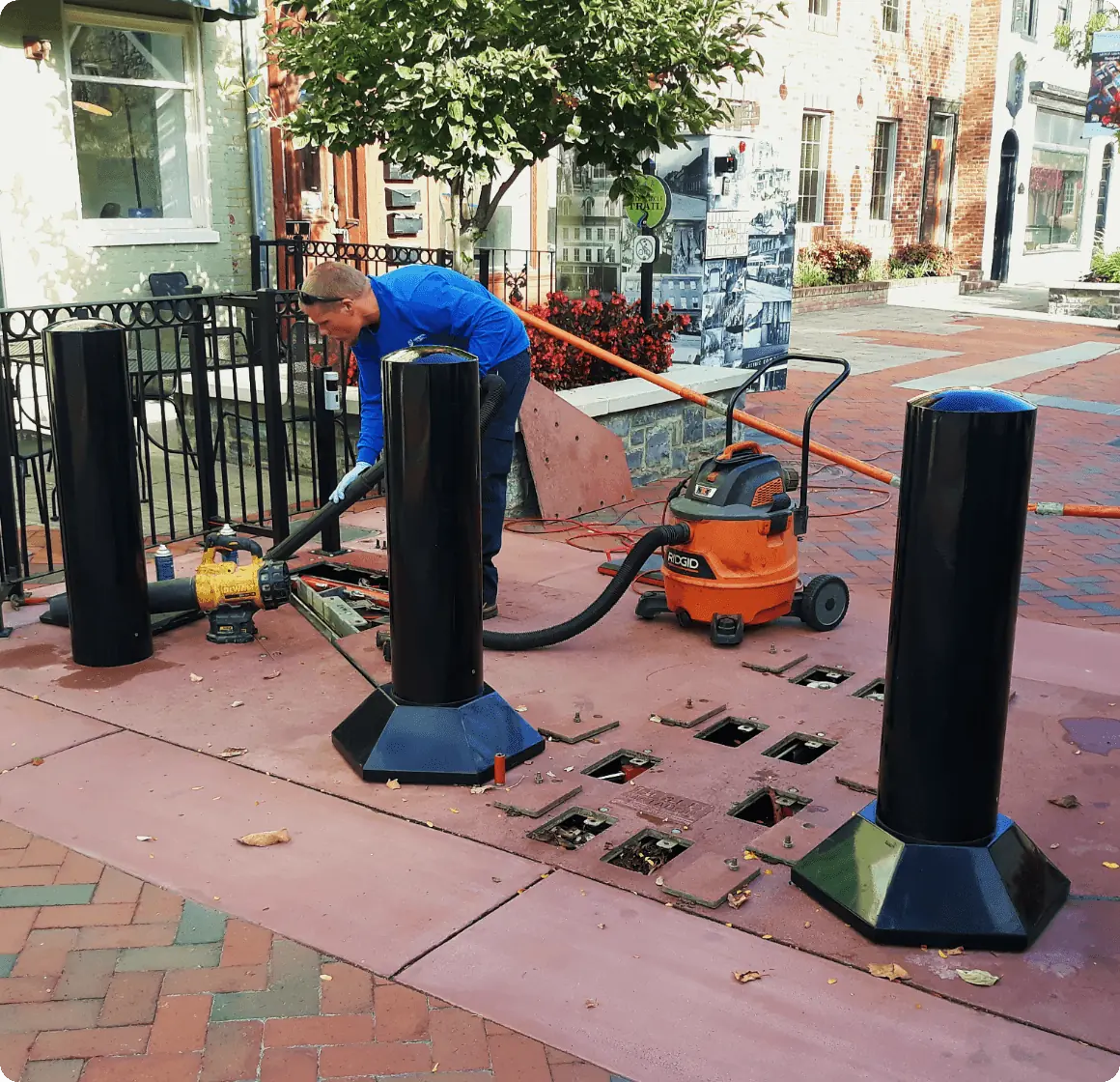 Technician in blue shirt installs bollards using tools and cleaning equipment.